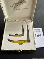 Open presentation box showing two yellow-handled folding knives and S&D Leopard branding