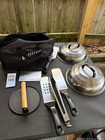 overview of grills accessories laid out including domes, press, utensils, scraper and bag