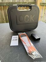 Front view of Glock molded plastic pistol case, packaged orange cable lock, magazine loader visible