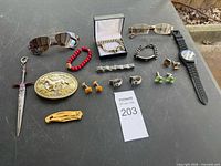 All items laid out including sunglasses, bracelets, watch, knife, cufflinks, tie bars, belt buckle, pendant