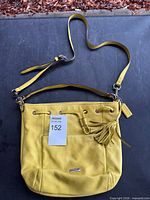 Front view of yellow Coach purse showing strap, front pocket, tassel, lot tag