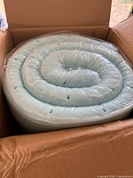 Rolled blue mattress topper sealed in plastic inside open box