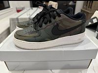 Side profile of both shoes showing camouflage upper, black Swoosh and white sole