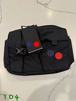 Front view of black Pinqponq messenger bag with hangtag and logo patches visible