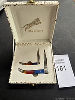 Closed presentation case open showing two folding knives inside, S&D Leopard logo visible
