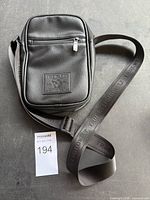 Front view of black True Religion leather sling bag showing strap and zipper pockets