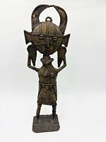 Front view of brass figure holding large mask-headdress