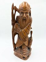 Front view of the wooden statue showing the elder figure, staff, and facial details