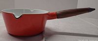 Side profile of red/orange enameled cast iron saucepan with wood handle