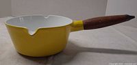 Side profile showing yellow exterior, white interior, one pour spout, wooden handle
