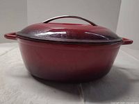 Side view of red enameled cast iron oval Dutch oven with lid attached