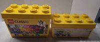 Two yellow LEGO storage brick boxes, one large with Classic sleeve, one small plain