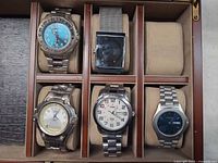 Five watches in wooden case showing dial designs and bracelets