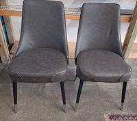 Front view of both gray faux leather dining chairs showing upholstery, legs, and chrome tips