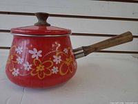 Side view of red floral enamel saucepan with wooden handle and lid