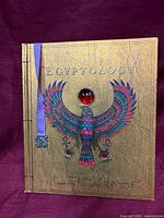 Front cover showing title, gold foil finish, winged scarab design, red gem, ribbon bookmark