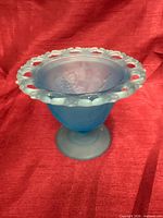 Front view of blue frosted glass compote showing grapes motif and open lace rim