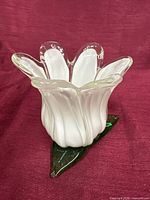 White blown glass flower-form votive holder on green leaf base, angled view