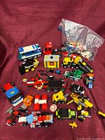 Wide shot showing all built LEGO vehicles, minifigures and bag of loose parts on burgundy background