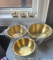 All six bowls and three spoons, showing unused condition and gold finish
