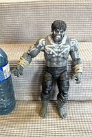 Front view of grey Hulk figure next to water bottle for scale