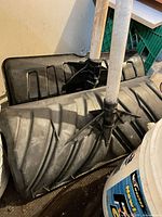 two black plastic snow shovels with wooden shafts leaning against wall