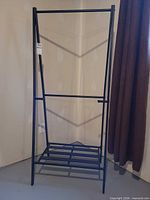 Front view of black metal garment rack with single rod and slatted bottom shelf