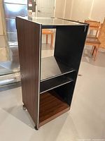 Full front-side view of narrow walnut veneer display cabinet showing glass top, interior shelf, chrome trim and casters