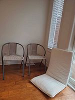 Two wicker chairs and one floor cushion near window