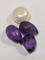 Three purple faceted pear stones and one round white drilled bead