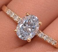 Close-up of ring on finger showing oval center stone and accent diamonds