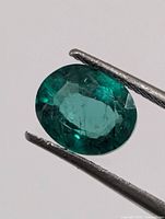 Front view of oval green created emerald held by tweezers
