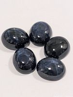 Five dark blue oval cabochon star sapphire gemstones arranged on white background