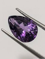 Close-up of pear-cut amethyst held in tweezers, showing faceting
