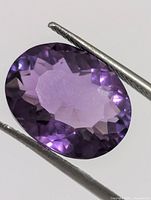 Front view of oval faceted purple amethyst held by tweezers