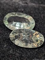 Two pale green oval faceted gemstones on black surface