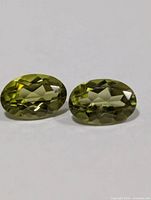 Two oval faceted olive-green peridot gemstones on white background