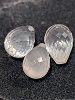 Three faceted pear-shape rose quartz gemstones on dark background