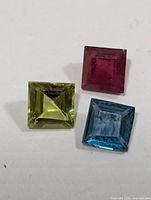 Three square-cut gemstones: green peridot, red ruby, blue topaz