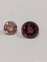 Two loose round faceted tourmaline gemstones on white background, showing size comparison and color variation