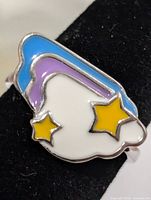 Oblique view of ring showing blue, purple, white cloud motif with two yellow stars
