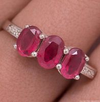 Top view of silver ring on finger showing three oval rubies and accent stones