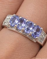 Close-up of ring on finger showing three central tanzanites and accent stones