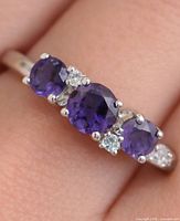 Close-up of silver ring on finger showing three amethysts and CZ accents