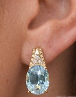 earring worn on ear showing scale, oval blue topaz and yellow-tone setting