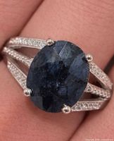 Top view of ring on finger showing oval dyed sapphire and split shank with topaz accents