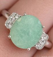 Top view of ring on finger displaying oval green dyed emerald and side topaz accents