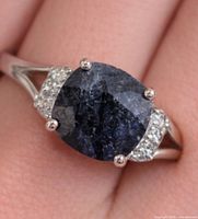 Earring with dark blue oval dyed sapphire and topaz accents on silver mount shown on finger