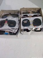 Two boxes filled with individually packaged clip-on sunglasses