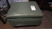 Top and front view of green faux leather footstool showing upholstery and legs